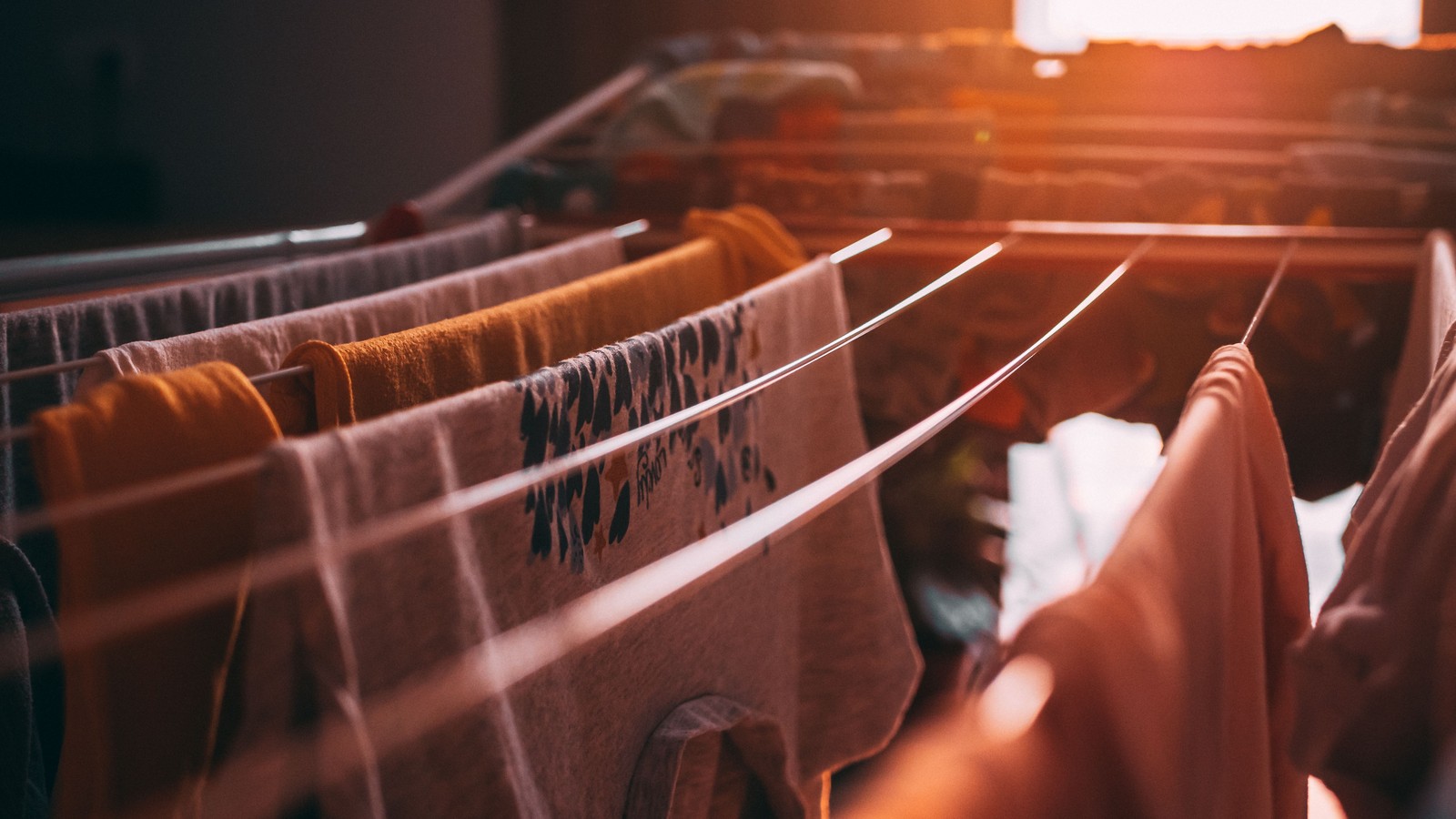 Clothes and towels hanging on an indoor drying rack in warm window light.