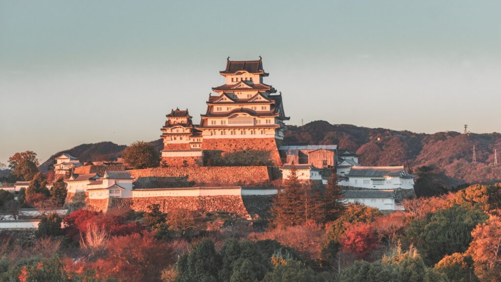 Himeji Castle in evening light with autumn foliage.