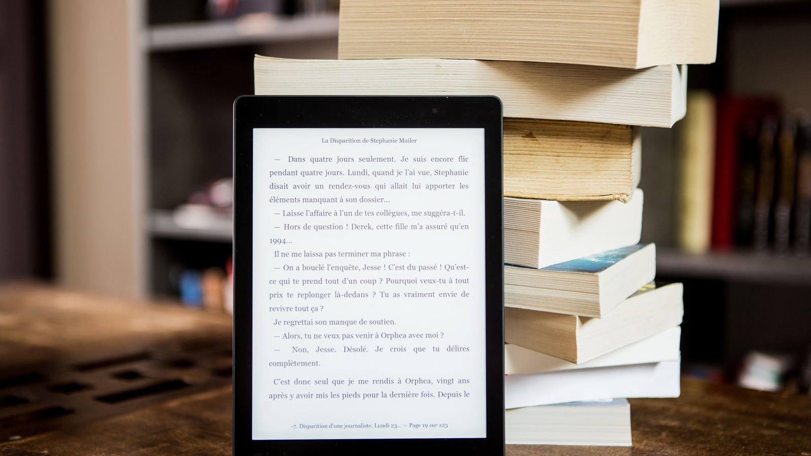 Black e-reader displaying text beside a stack of printed books
