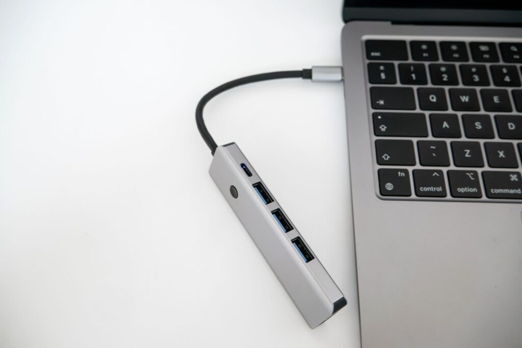 A silver USB hub connected by a black cable to a laptop on a white desk