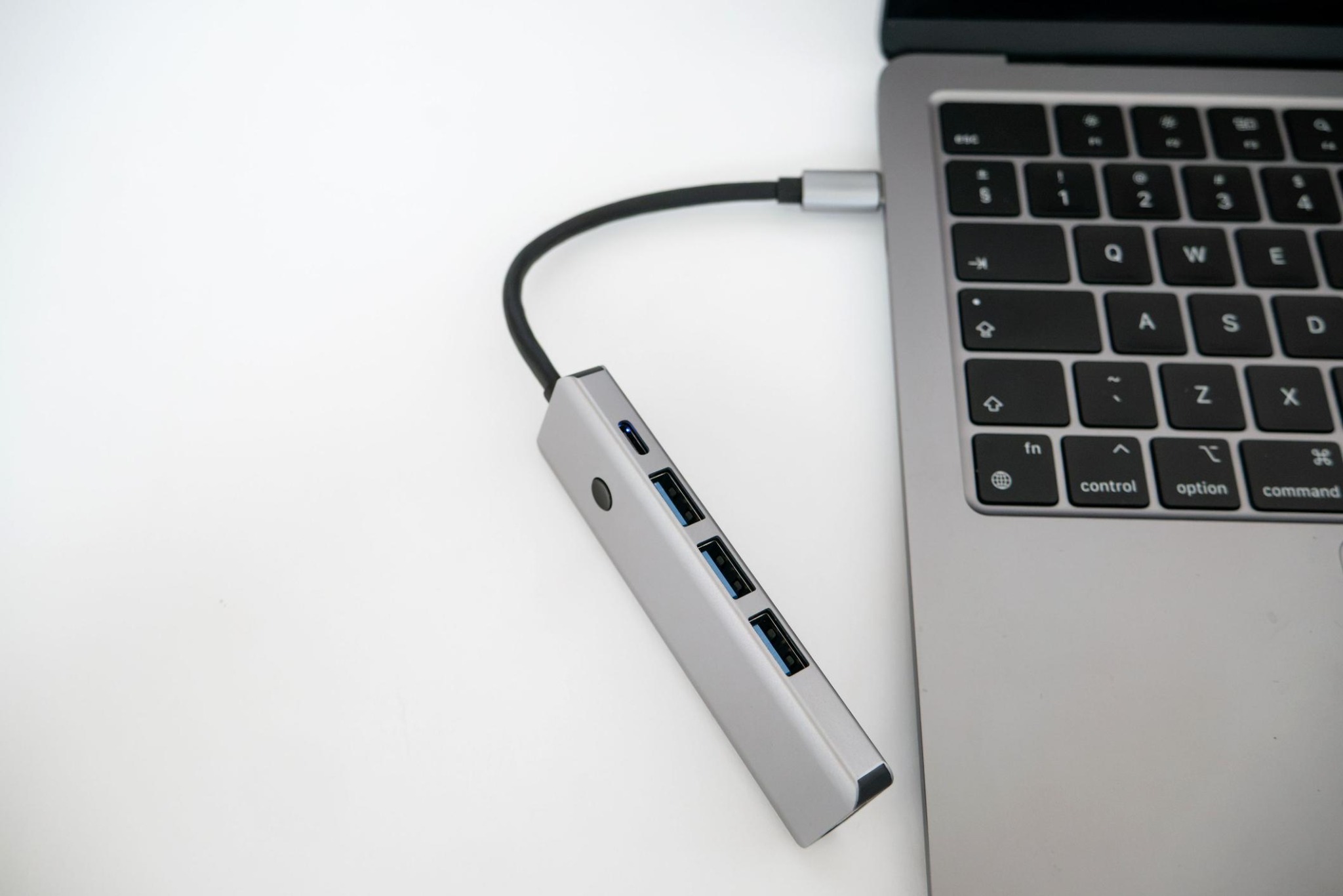 A silver USB hub connected by a black cable to a laptop on a white desk