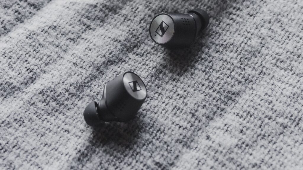 Two black wireless earbuds on textured grey fabric