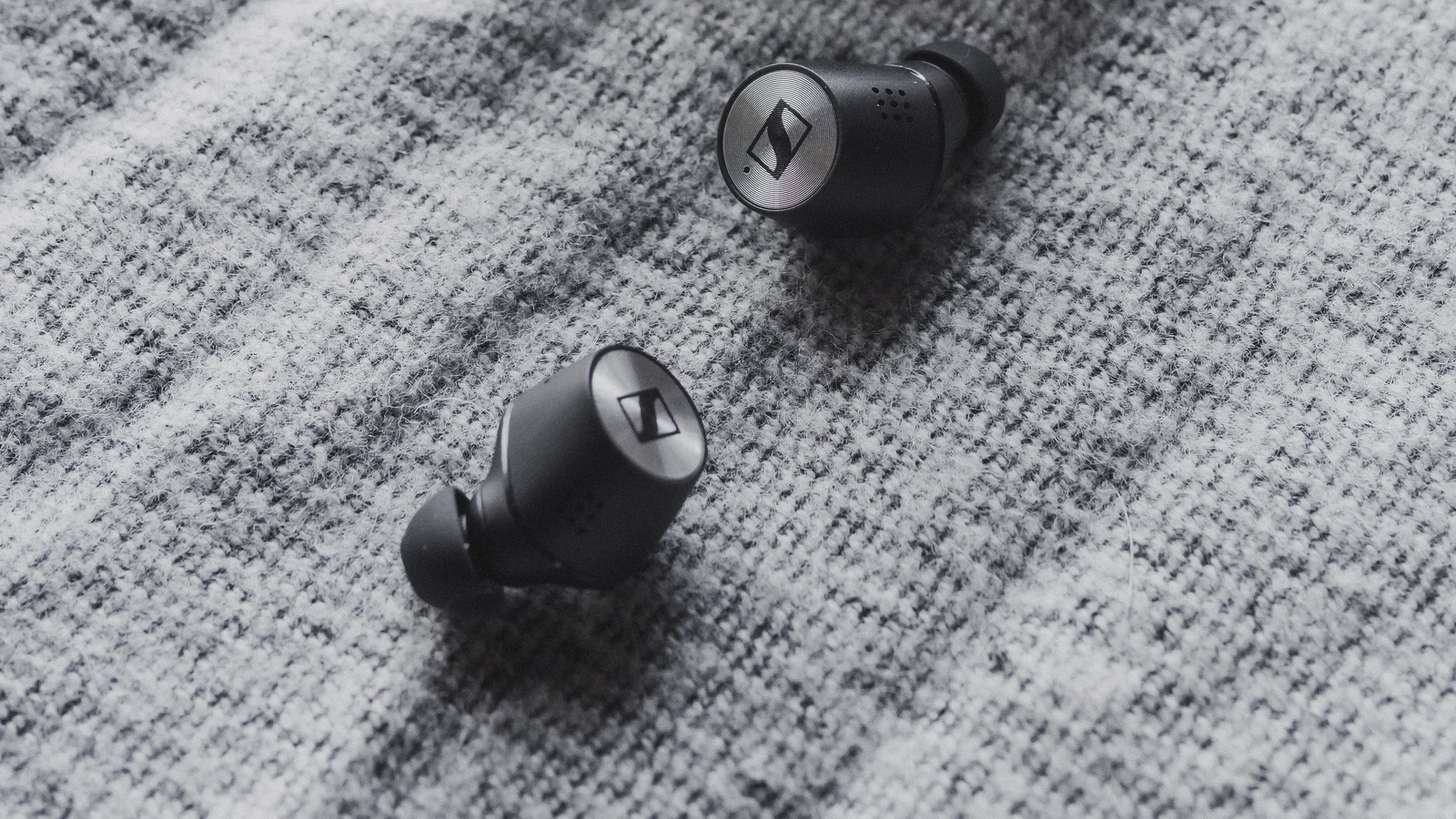 Two black wireless earbuds on textured grey fabric